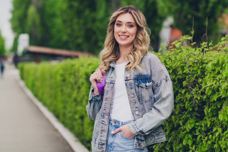 Ritratto di una giovane e graziosa zainetta con un sorriso e una giacca di jeans viaggia per strada fuori immagini stock