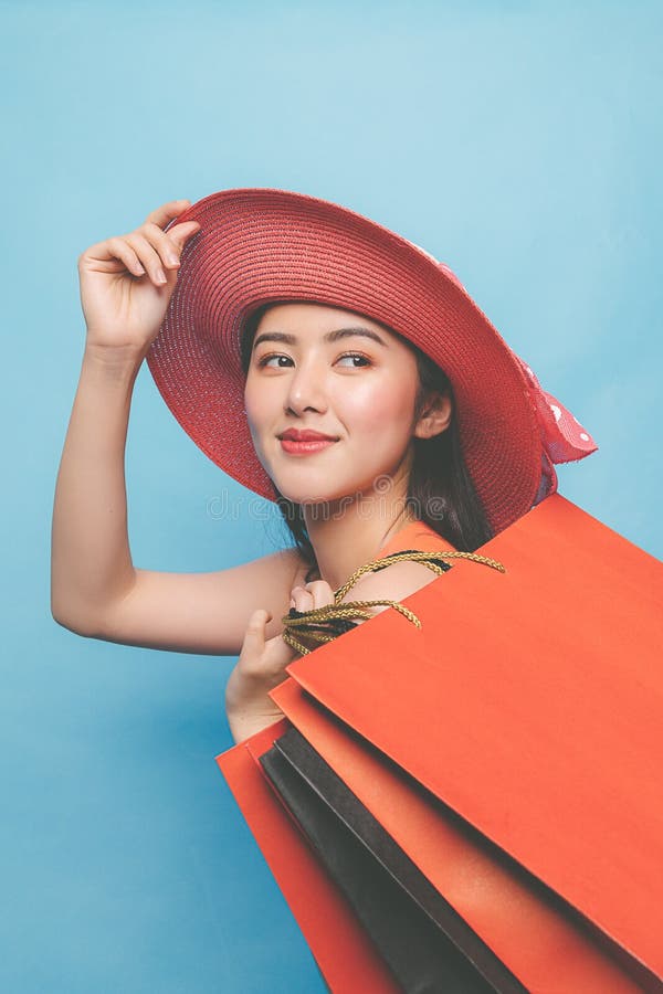 Ritratto di una giovane ragazza asiatica che indossa abiti e cappello da sole e tiene le borse della spesa fotografia stock libera da diritti Ritratto di una giovane ragazza asiatica che indossa abiti e cappello da sole e tiene le borse della spesa fotografia stock libera da diritti
