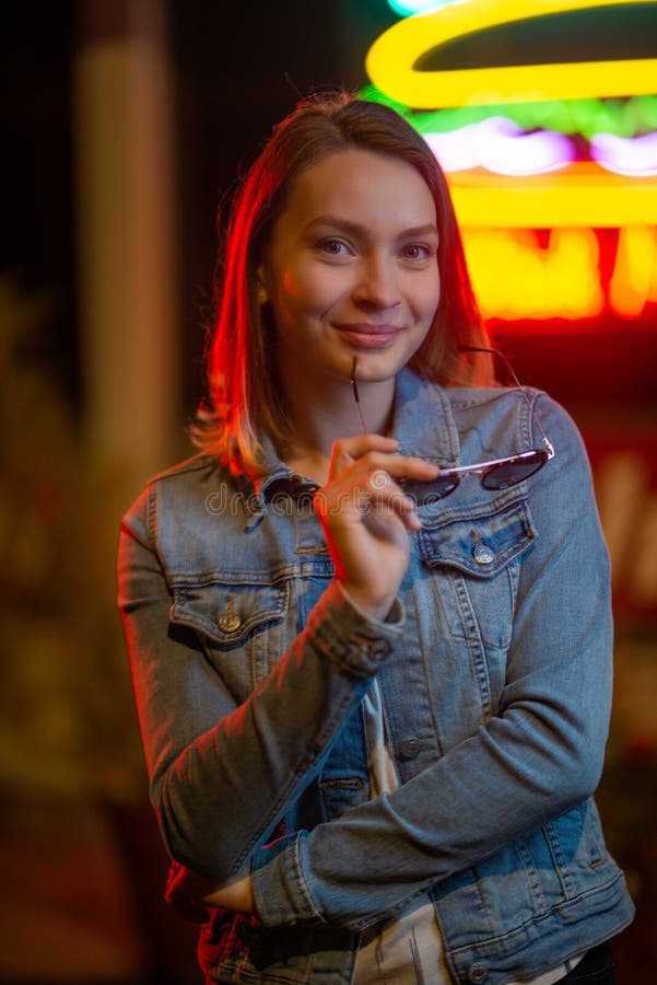 Ritratto di una giovane ragazza con occhiali da sole, con luce creativa sullo sfondo di lampade al neon immagine stock libera da diritti Ritratto di una giovane ragazza con occhiali da sole, con luce creativa sullo sfondo di lampade al neon immagine stock libera da diritti