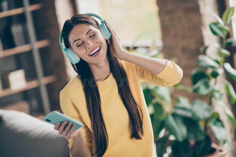 Ritratto di una ragazza allegra e positiva ascolta della musica sul suo smartphone sceglie la melodia gustare un maglione giallo