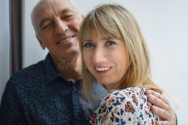Ritratto felice adorabile dell'uomo anziano che abbraccia la sua giovane moglie sorridente bionda-dai capelli che porta vestito c fotografia stock libera da diritti Ritratto felice adorabile dell'uomo anziano che abbraccia la sua giovane moglie sorridente bionda-dai capelli che porta vestito c fotografia stock libera da diritti