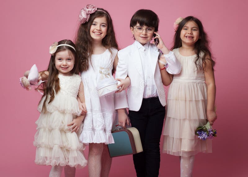 Ritratto frontale di un gruppo di bambini felici vestiti in bello abbigliamento classico, isolato su fondo rosa fotografia stock libera da diritti Ritratto frontale di un gruppo di bambini felici vestiti in bello abbigliamento classico, isolato su fondo rosa fotografia stock libera da diritti