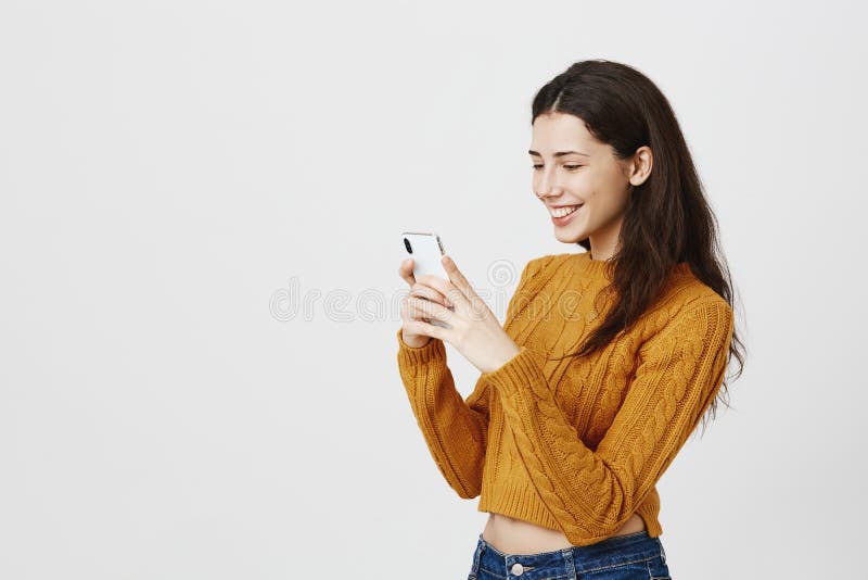 ritratto Mezzo girato della foto femminile sveglia alla moda di presa o di messaggio sullo smartphone mentre sorridendo largament immagini stock ritratto Mezzo girato della foto femminile sveglia alla moda di presa o di messaggio sullo smartphone mentre sorridendo largament immagini stock