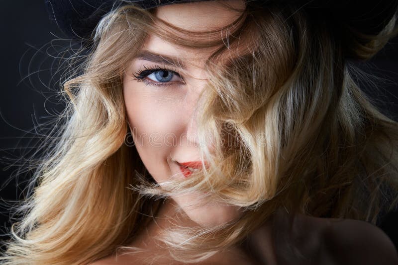 Ritratto scuro della donna bionda di fascino, portando un cappello, guardante in camera, colpo dello studio, fondo vago, luce di fotografie stock libere da diritti Ritratto scuro della donna bionda di fascino, portando un cappello, guardante in camera, colpo dello studio, fondo vago, luce di fotografie stock libere da diritti