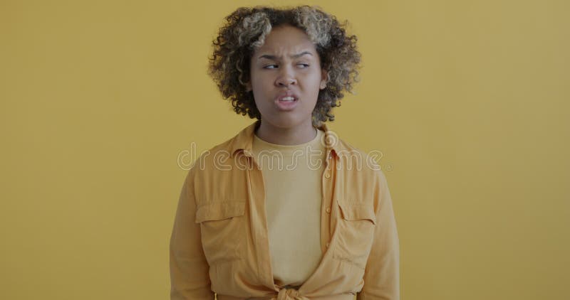Ritratto in slow motion di una donna africana frustrata e confusa che trema la testa incrociando le braccia su fondo giallo
