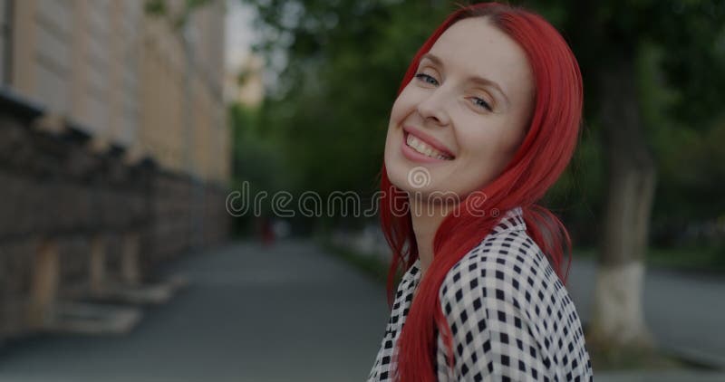 Ritratto in slow motion di una giovane donna di bell'aspetto con i capelli rossi tinti che gira verso la telecamera e che sorride