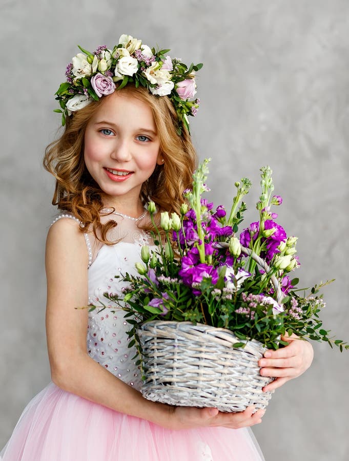 Ritratto verticale di bella bambina sveglia in una corona dei fiori freschi sulla sua testa ed in un canestro di bella molla fotografia stock Ritratto verticale di bella bambina sveglia in una corona dei fiori freschi sulla sua testa ed in un canestro di bella molla fotografia stock