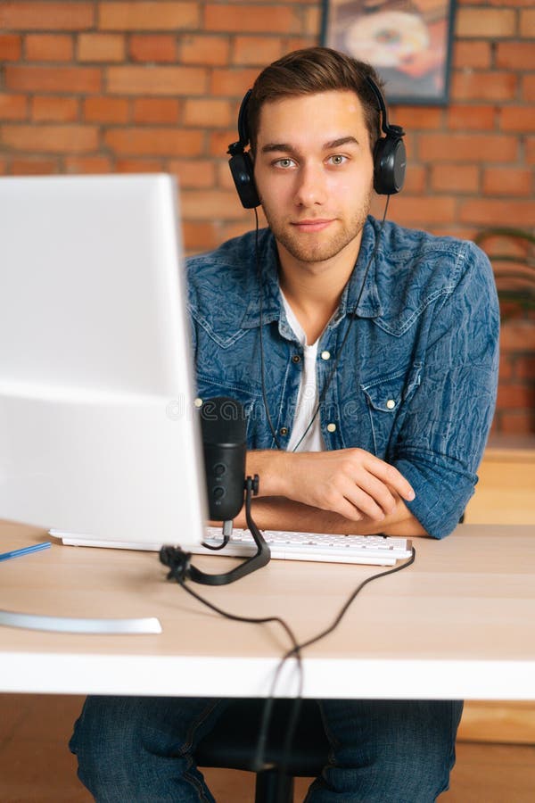 Ritratto verticale di un bell'audio blogger seducente maschio che indossa cuffie sedute alla scrivania con professionale fotografia stock