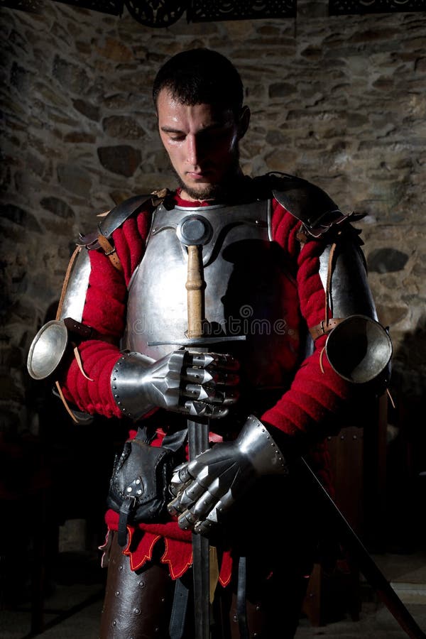 Ritter Standing With Head gebeugt im Gebet und im Halten der Metallklinge gegen alte Steinwand stockfotografie Ritter Standing With Head gebeugt im Gebet und im Halten der Metallklinge gegen alte Steinwand stockfotografie