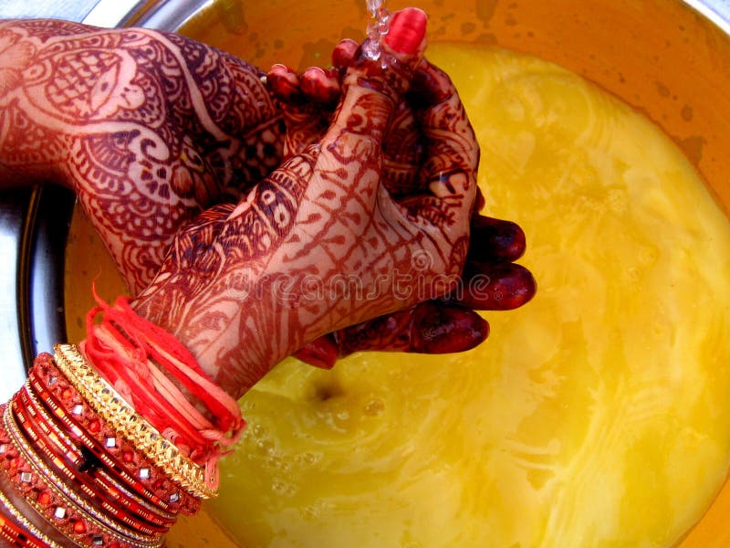 A groom and his bride wash their mehendi applied hands in the same bowl with haldi(turmeric powder) as a part of a ritual in Indian Marriages. A groom and his bride wash their mehendi applied hands in the same bowl with haldi(turmeric powder) as a part of a ritual in Indian Marriages.