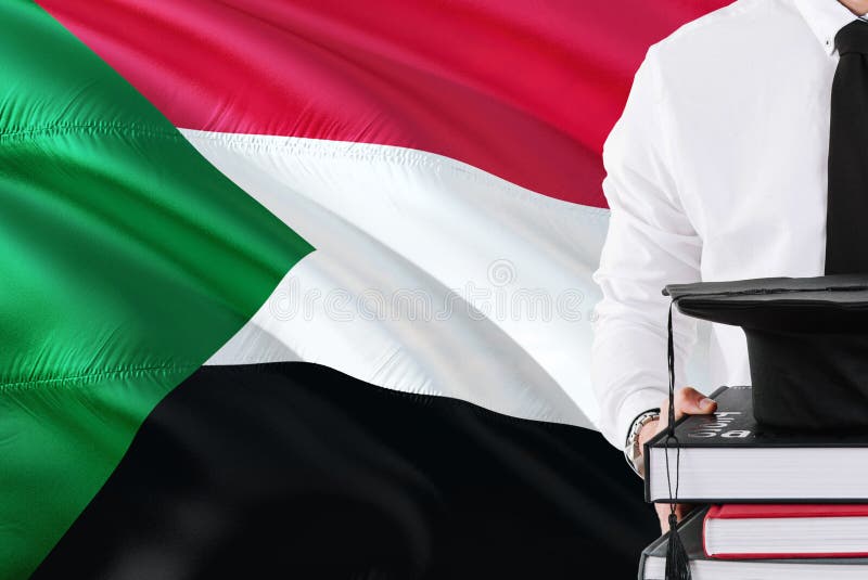 Riuscito concetto sudanese di istruzione dello studente Tenuta i libri e del cappuccio di graduazione sopra il fondo della bandie fotografie stock Riuscito concetto sudanese di istruzione dello studente Tenuta i libri e del cappuccio di graduazione sopra il fondo della bandie fotografie stock