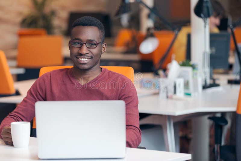 Riuscito uomo afroamericano sorridente bello che per mezzo del computer portatile fotografia stock Riuscito uomo afroamericano sorridente bello che per mezzo del computer portatile fotografia stock