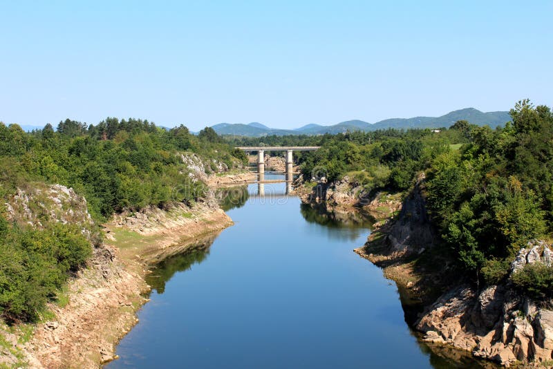 Rivier met lage de zomerwaterspiegels die naar concrete brug stromen die met weelderige groene bosvegetatie wordt omringd royalty-vrije stock afbeeldingen Rivier met lage de zomerwaterspiegels die naar concrete brug stromen die met weelderige groene bosvegetatie wordt omringd royalty-vrije stock afbeeldingen