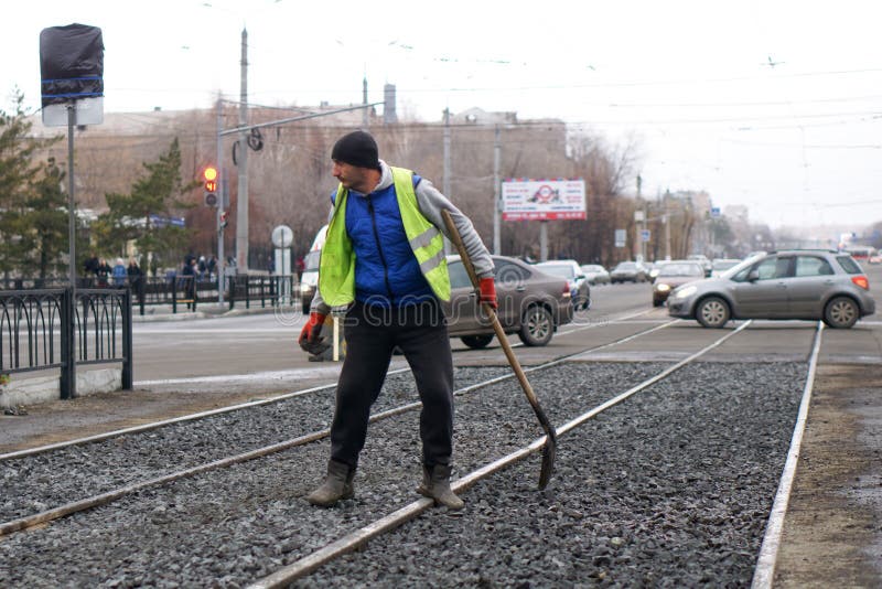A road worker in a yellow vest is rubbing rubble on the territory near the tram stop. November 7, 2019. Magnitogorsk, Russia royalty free stock photos A road worker in a yellow vest is rubbing rubble on the territory near the tram stop. November 7, 2019. Magnitogorsk, Russia royalty free stock photos