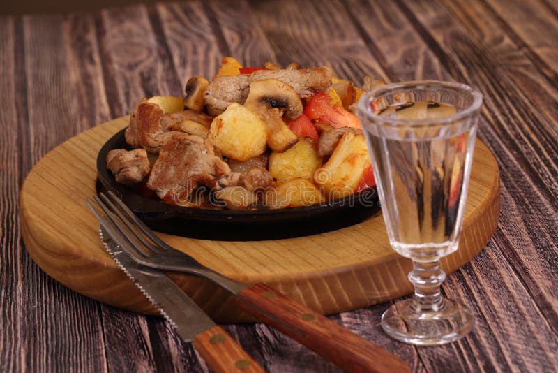 Roast with a potato, meat and mushrooms and a vodka wine-glass