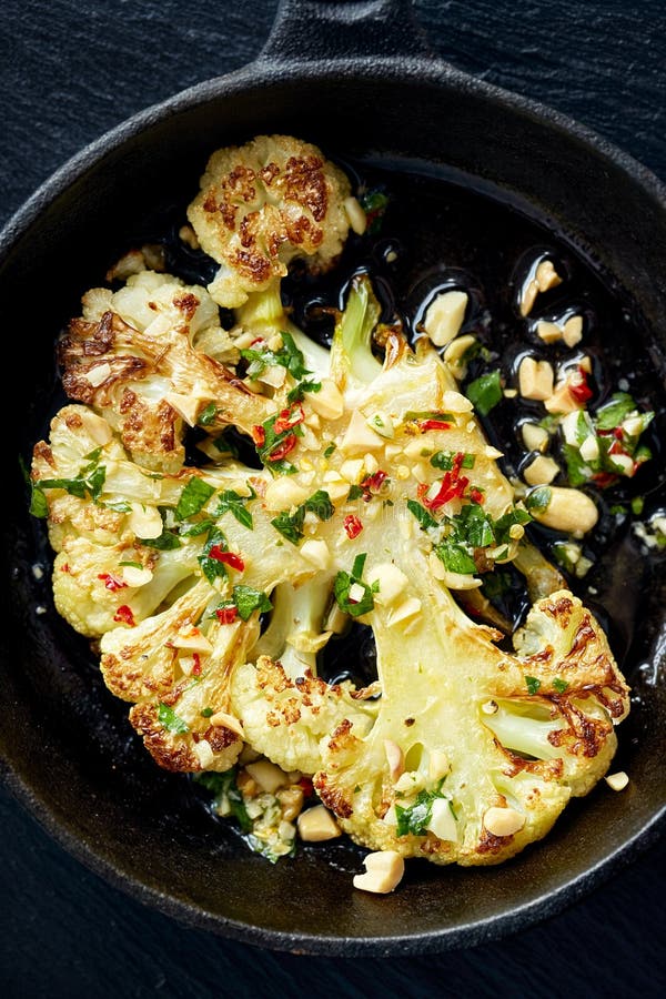 Roasted cauliflower steak with the addition dip with peanuts, chili and fresh parsley on iron frying pan