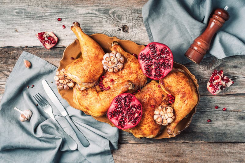 Roasted chicken with pomegranate and garlic on wooden background. Friends or family dinner. Festive Christmas table. Top view.