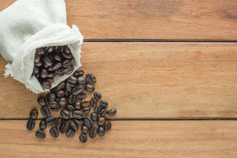 Roasted dark coffee beans in sack on wooden background.