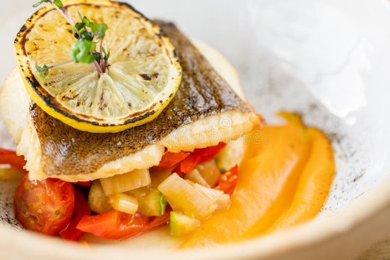 Roasted pike perch or cod fish with baked vegetables. Dish decorated with a slice of lemon. Restaurant menu stock images