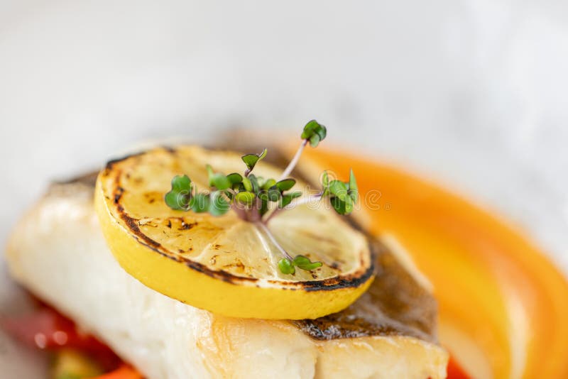Roasted pike perch or cod fish with baked vegetables. Dish decorated with a slice of lemon. Restaurant menu stock photos