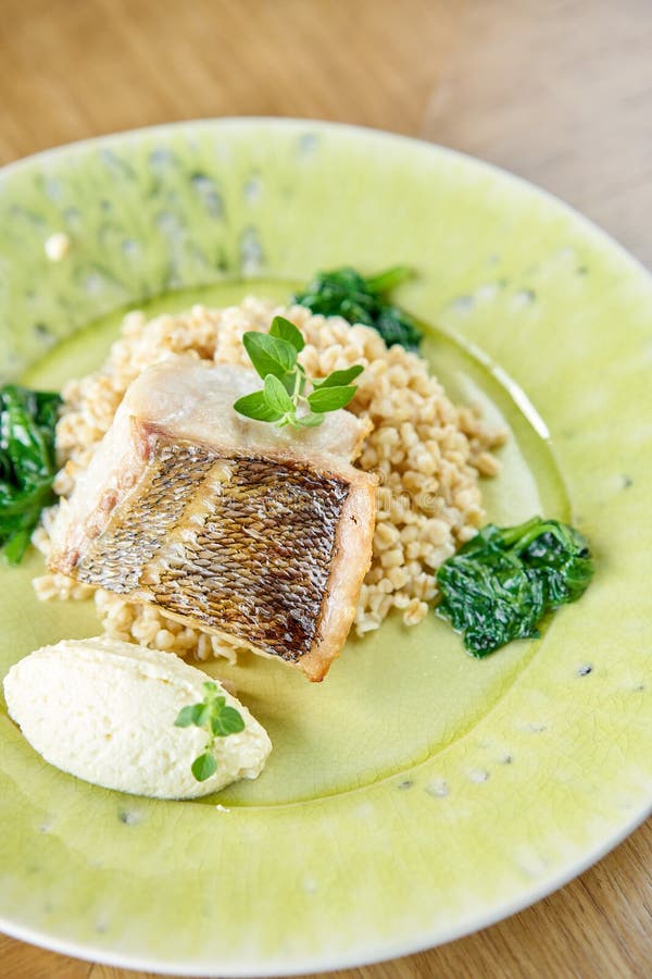 Roasted pike perch or cod fish with bulgur. Dish decorated with a spinach. Restaurant menu royalty free stock images
