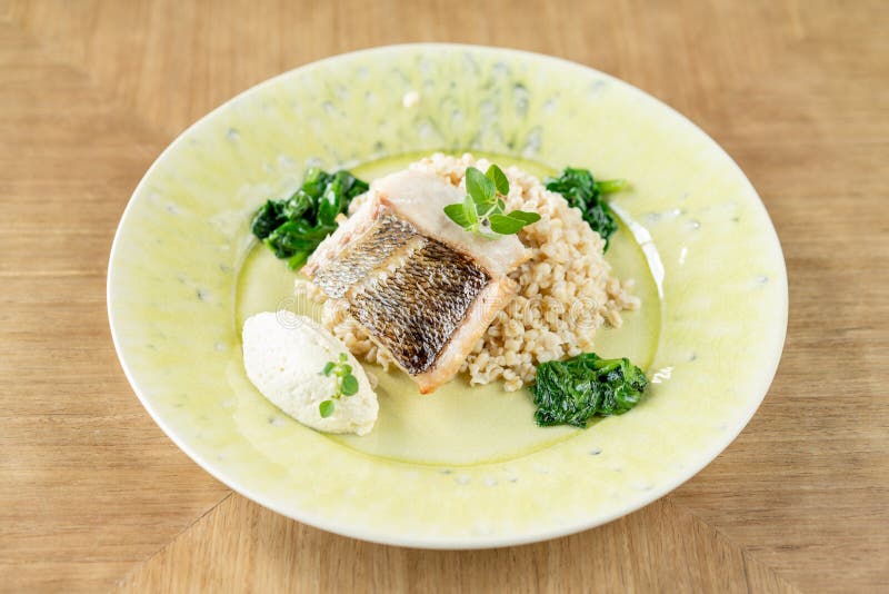 Roasted pike perch or cod fish with bulgur. Dish decorated with a spinach. Restaurant menu stock photo