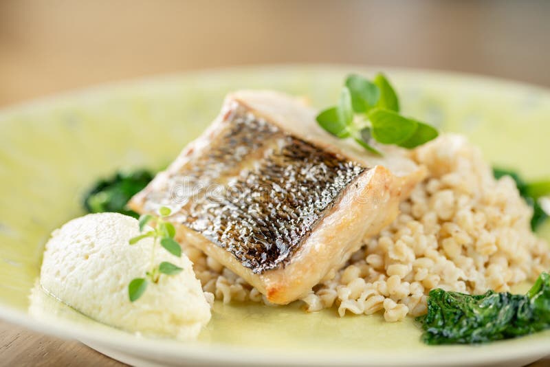 Roasted pike perch or cod fish with bulgur. Dish decorated with a spinach. Restaurant menu stock image