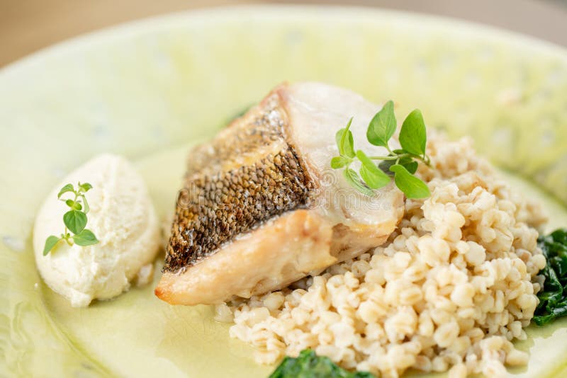 Roasted pike perch or cod fish with bulgur. Dish decorated with a spinach. Restaurant menu stock photography