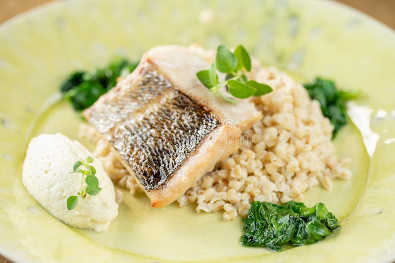 Roasted pike perch or cod fish with bulgur. Dish decorated with a spinach. Restaurant menu royalty free stock image