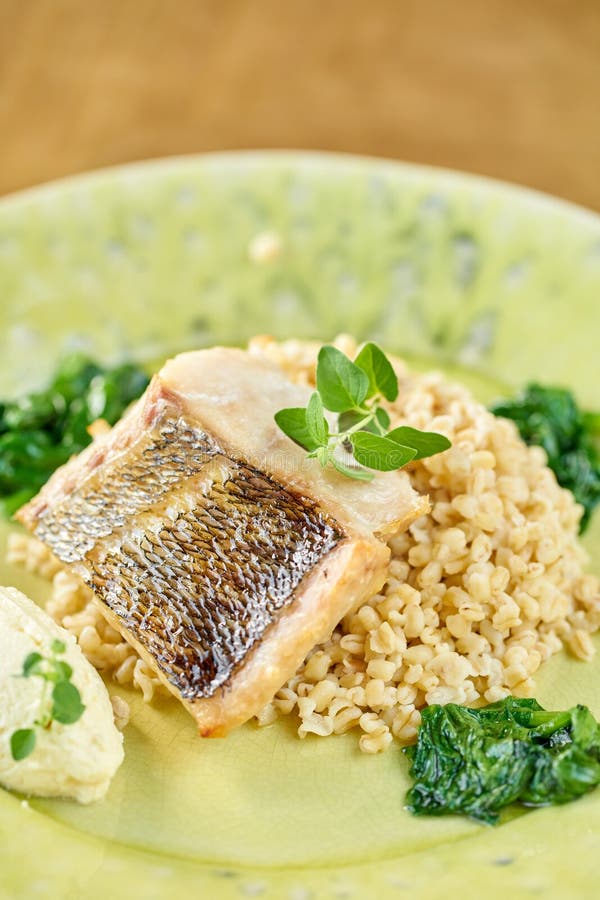 Roasted Pike perch with spelt and Polish sauce. Dish decorated with a spinach. Restaurant menu royalty free stock photography