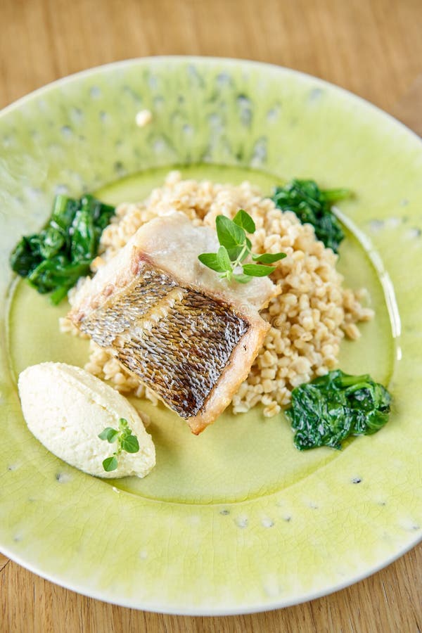 Roasted Pike perch with spelt and Polish sauce. Dish decorated with a spinach. Restaurant menu royalty free stock images