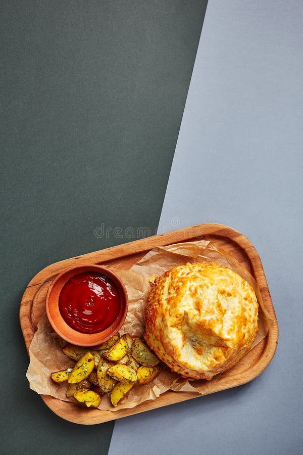 Roasted round cheese loaf and fried potatoes. Restaurant dish portion. Fast food serving with tomato sauce on wooden tray side view. Cafe quick meal close up royalty free stock image Roasted round cheese loaf and fried potatoes. Restaurant dish portion. Fast food serving with tomato sauce on wooden tray side view. Cafe quick meal close up royalty free stock image