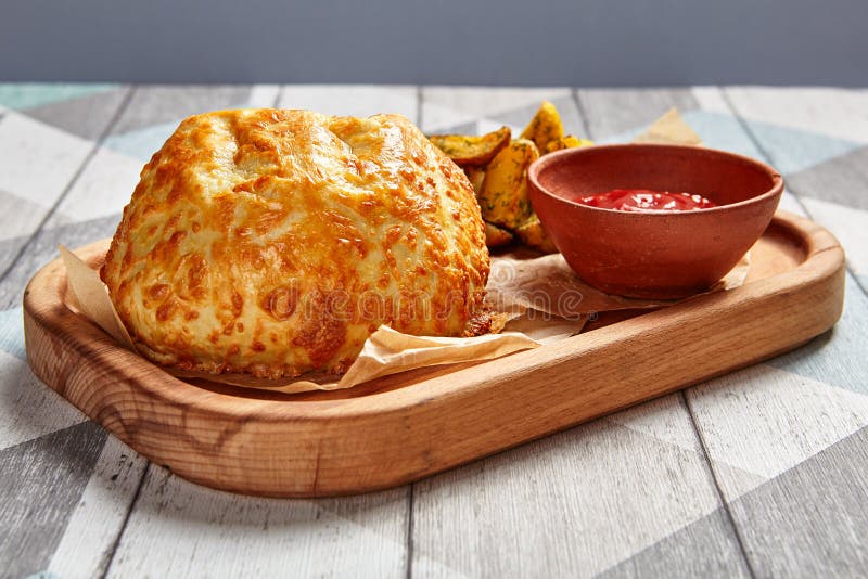 Roasted round cheese loaf and fried potatoes. Restaurant dish portion. Fast food serving with tomato sauce on wooden tray side view. Cafe quick meal close up royalty free stock photo Roasted round cheese loaf and fried potatoes. Restaurant dish portion. Fast food serving with tomato sauce on wooden tray side view. Cafe quick meal close up royalty free stock photo