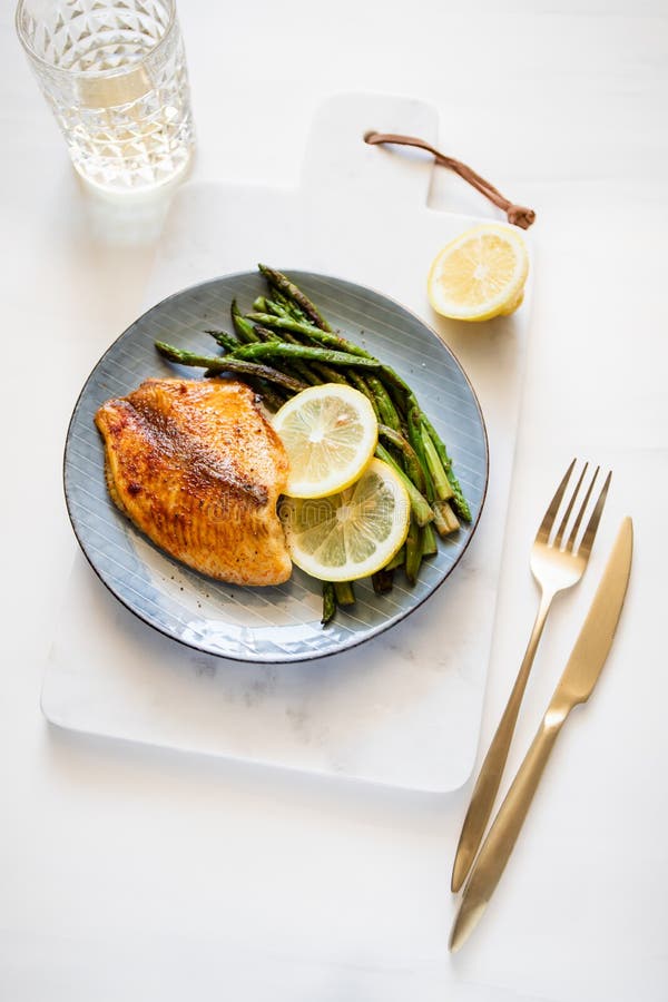 Roasted tilapia fish with asparagus on a ceramic plate.