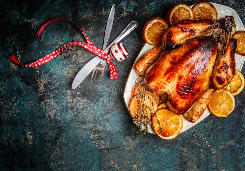Roasted turkey or chicken with orange slices in plate for Christmas dinner served with fork,knife and festive decoration on dark r