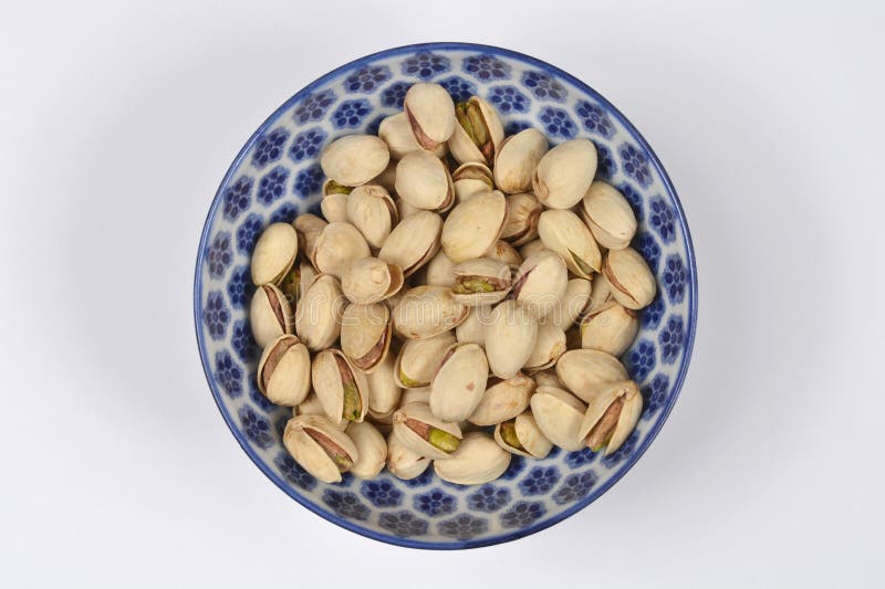 A top view of roasted unsalted pistachios in their shells served in a blue and white patterned ceramic bowl on a white background. Pistachios served stock images, royalty-free photos and pictures
