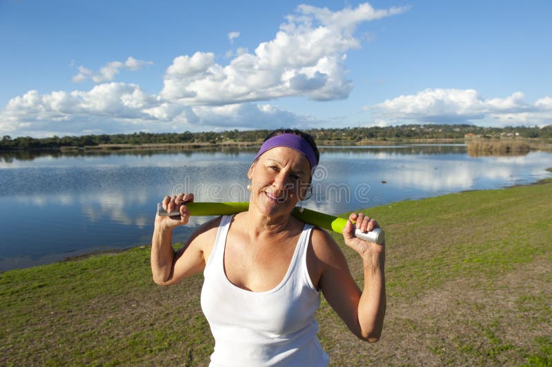 A healthy and fit mature woman in a relaxed and happy pose after exercising with weights at a lake. A healthy and fit mature woman in a relaxed and happy pose after exercising with weights at a lake.