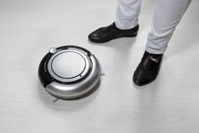 Robot vacuum on white wooden floor and legs of happy maid or housewife. Smart home concept stock image