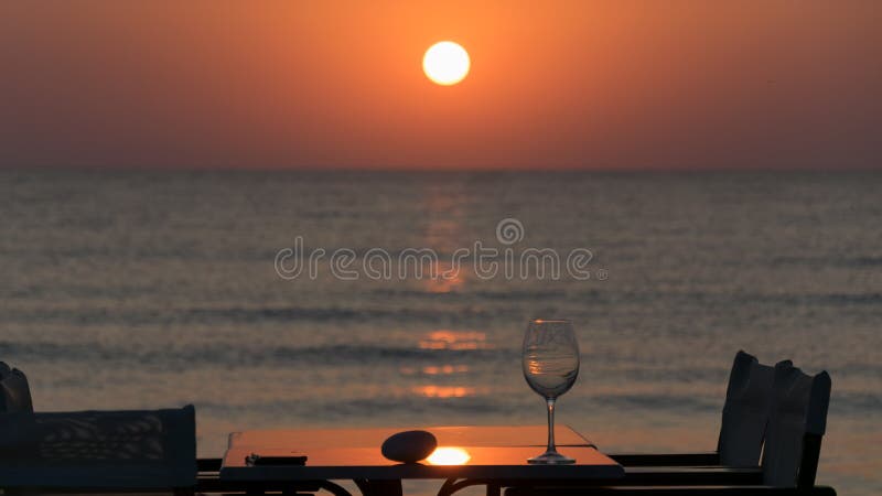 Roca y vidrio en una tabla con las sillas y el paraguas en caña, en la salida del sol en el mar Mediterráneo fotografía de archivo libre de regalías Roca y vidrio en una tabla con las sillas y el paraguas en caña, en la salida del sol en el mar Mediterráneo fotografía de archivo libre de regalías