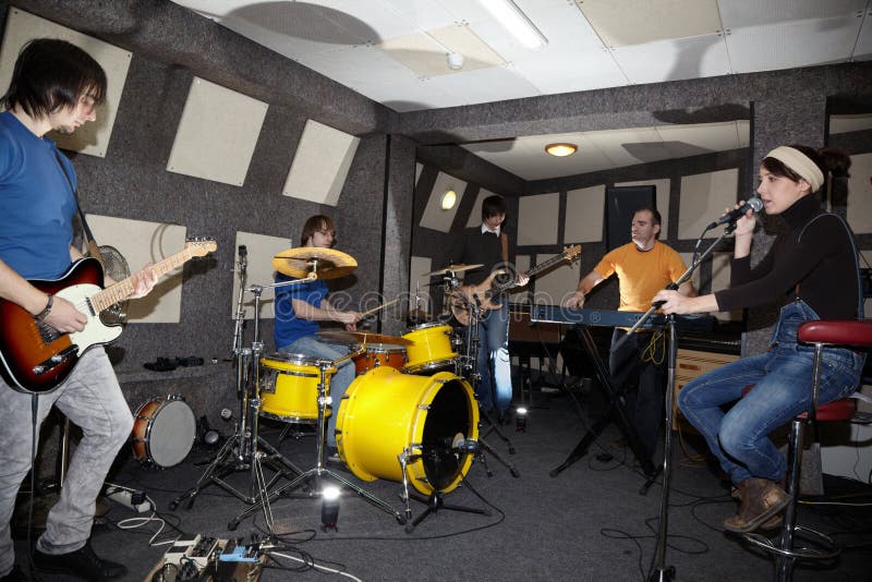 A rock band. vocalist girl, two musicians with electro guitars, keyboarder and one drummer working in studio. flashes in center. A rock band. vocalist girl, two musicians with electro guitars, keyboarder and one drummer working in studio. flashes in center