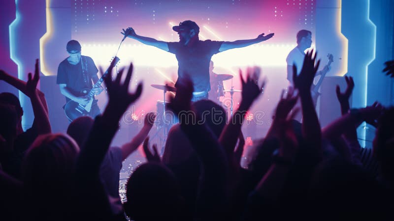 Rock Band with Guitarists and Drummer Performing at a Concert in a Night Club. Front Row Crowd is