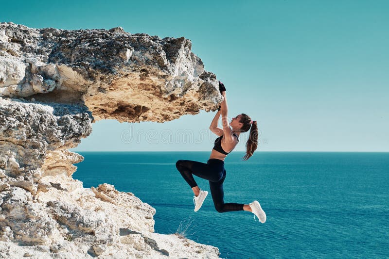 Rock climbing. Sport. Active lifestyle. Athlete woman hangs on sharp cliff. Seascape. Outdoors workout. High resilience
