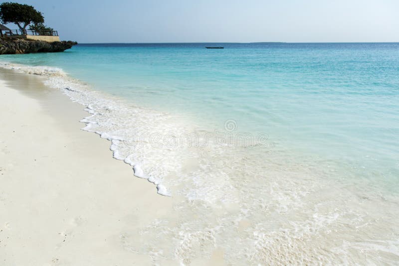 Clean white sand beach with turquoise water . Tropical island background. Small waves crushing on the beach. Clean empty white sand beach on Zanzibar. Rock on the beach. Clean white sand beach with turquoise water . Tropical island background. Small waves crushing on the beach. Clean empty white sand beach on Zanzibar. Rock on the beach