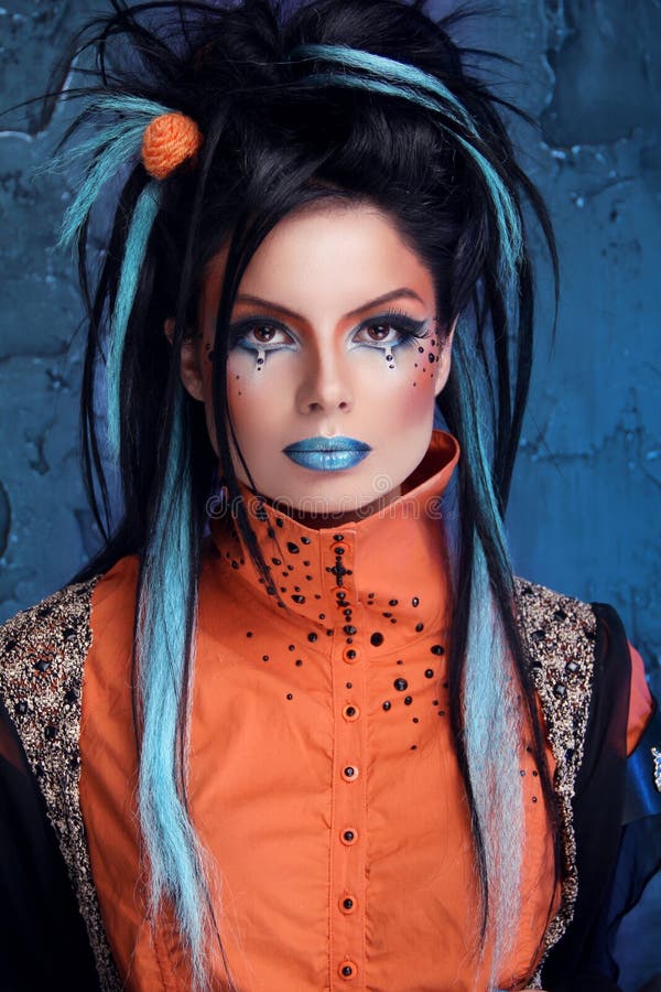 Rock girl with blue lips and punk hairstyle leaning against grunge wall