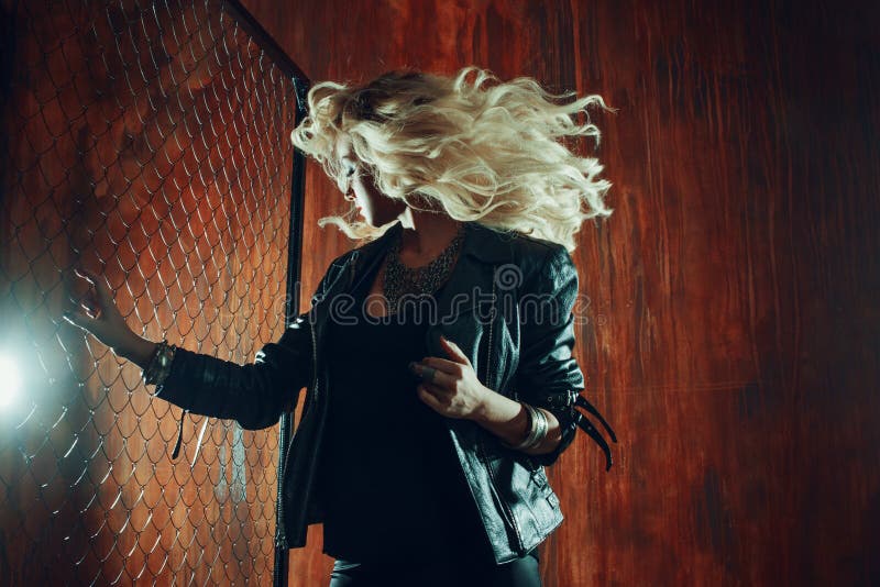 Rock`n`roll girl, young beautiful woman dances in dark alley, against the fence mesh