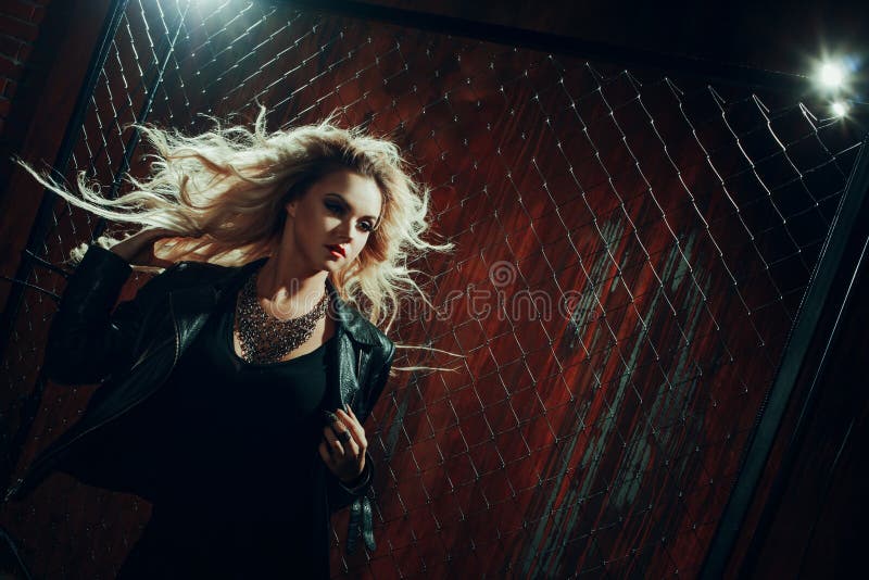 Rock`n`roll girl, young beautiful woman dances in dark alley, against the fence mesh