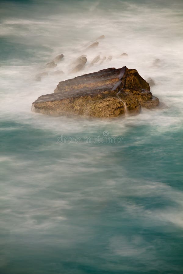 Rock in ocean enveloped by waves in long exposure