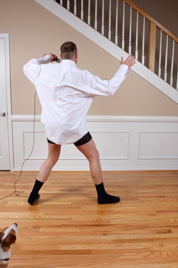 A man having too much fun sliding on the wood floors with his microphone. Notice cute dog in left corner watching. A man having too much fun sliding on the wood floors with his microphone. Notice cute dog in left corner watching.