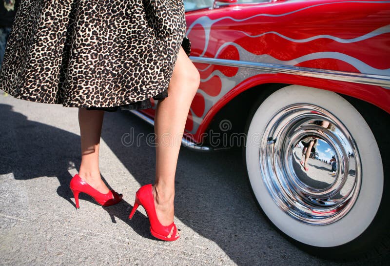 Žena, oblečená ako Rockabilly, hip kultúry 1950 štýl, stojí vedľa červené svalové auto s whitewalls.