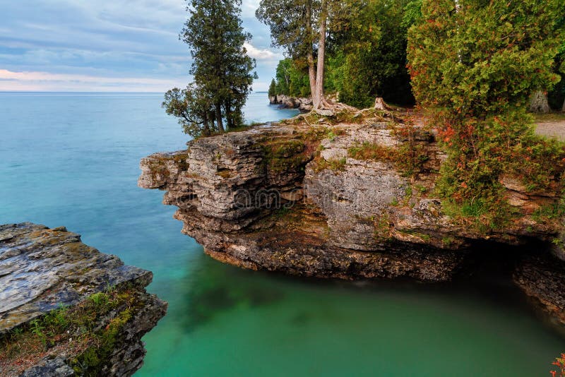 Early morning long exposure photo at Door County, Wisconsin's Cave Point, on Lake Michigan, reveals rocky cliffs, colorful waters, and a cloudy sky. Early morning long exposure photo at Door County, Wisconsin's Cave Point, on Lake Michigan, reveals rocky cliffs, colorful waters, and a cloudy sky.